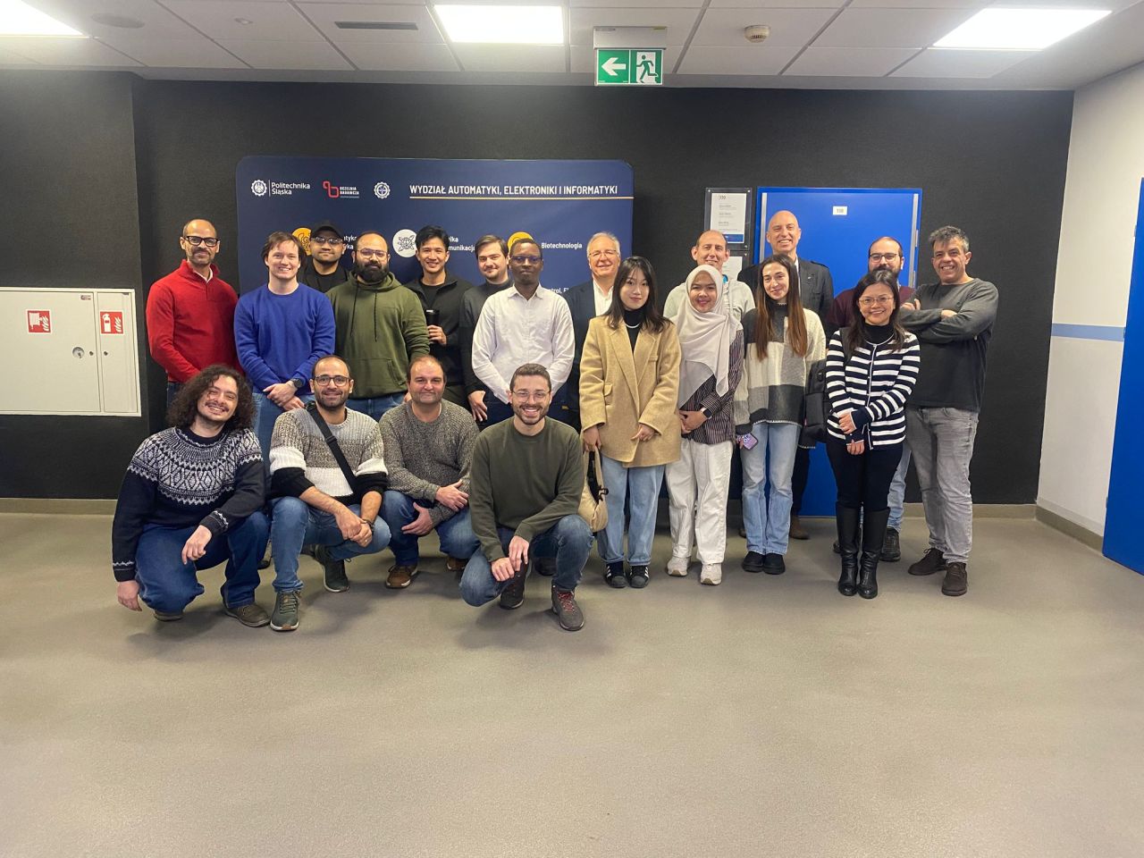 A group of smiling people pose in front of a dark blue poster.